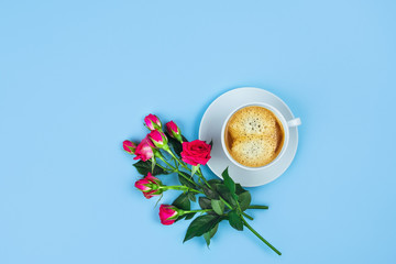 Morning Cup of coffee and a beautiful roses on blue background, top view.