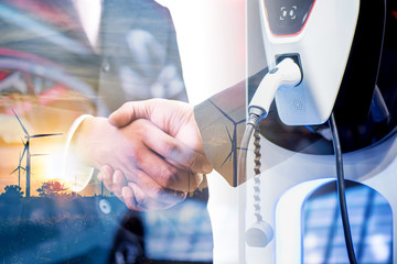 double exposure of business handshake and silhouette of wind turbine at sunset with electric car bat