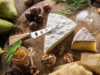 Wall Mural - Cheese platter with organic cheeses, fruits, nuts and wine on wooden background. Top view. Tasty cheese starter.