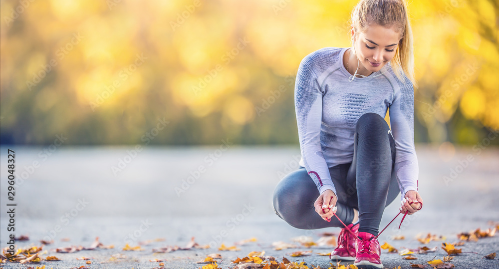 Woman runner tying shoelaces before jogging in autumn tree alley park. Sports female autumn outfit leggings and thermal underwear - obrazy, fototapety, plakaty 