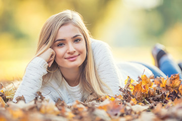 Wall Mural - Autumn portrait of young woman lying on maple leaves in park