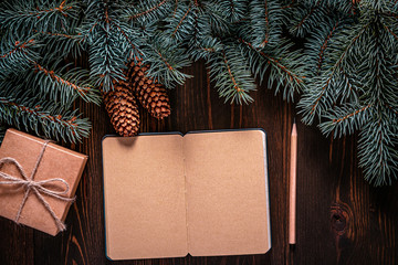 Wall Mural - Christmas frame from fir branches on a background of an old brown board around an open notebook with blank sheets. Frame of fir branches. Christmas card blank concept.