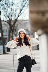 Wall Mural - Elegant girl in a winter city. Woman in a white knited sweater. Beautiful lady with dark hair.