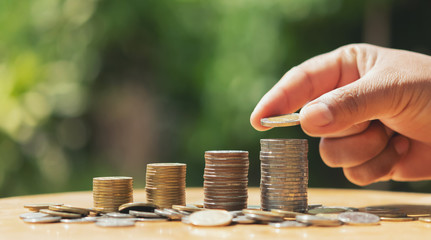 saving money hand putting coins on stack on table with sunshine. concept finance and accounting