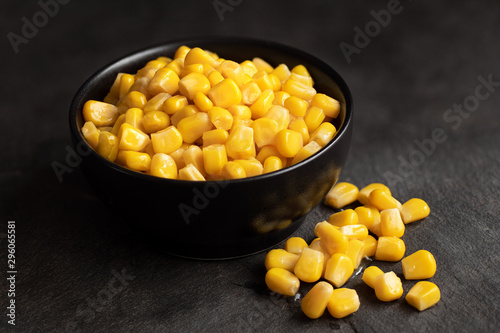 Fotomural Canned sweet corn in a black ceramic bowl isolated on black slate next to spilled sweet corn