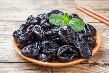 Bowl with tasty dried plums on wooden table