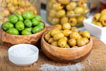 Raw olives and marinated olives in bowl with salt on wooden background.