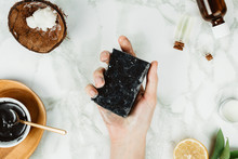 Flatlay Of Woman's Hands Holding Homemade Charcoal Soap With Its Ingredients On The Side, Natural Home Beauty Concept