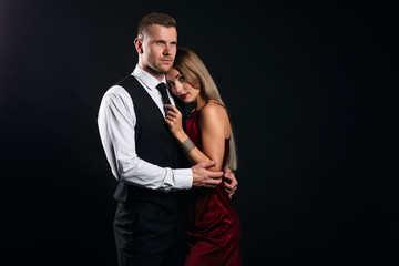 Wall Mural - young man in fashion suit embracing his week woman, protecting her, isolated black background, studio shot. protection, deffence, copy space