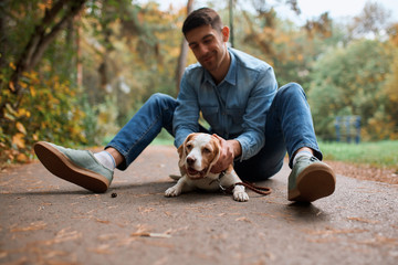 cheerful young handsome man sitting on the road with his adorle pet, enjoying time in the fresh air. full length photo. friendship