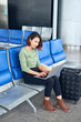 © makistock - Asian Woman using laptop computer at airport terminal sitting with luggage suitcase for travel