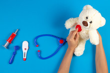 Kid Hands With Toy Stethoscope, Teddy Bear And Toy Medicine Tools On Light Blue Background. Children Doctor, Medicine Concept