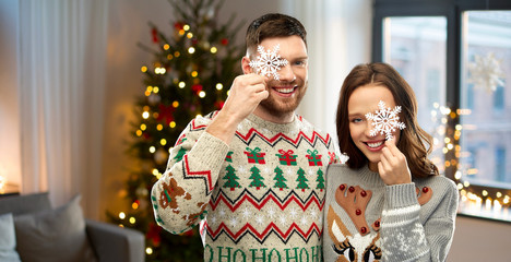 Poster - christmas, people and holidays concept - portrait of happy couple at ugly sweater party with snowflakes over home background