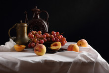 Peaches, Grapes And Vintage Jugs On A White Tablecloth