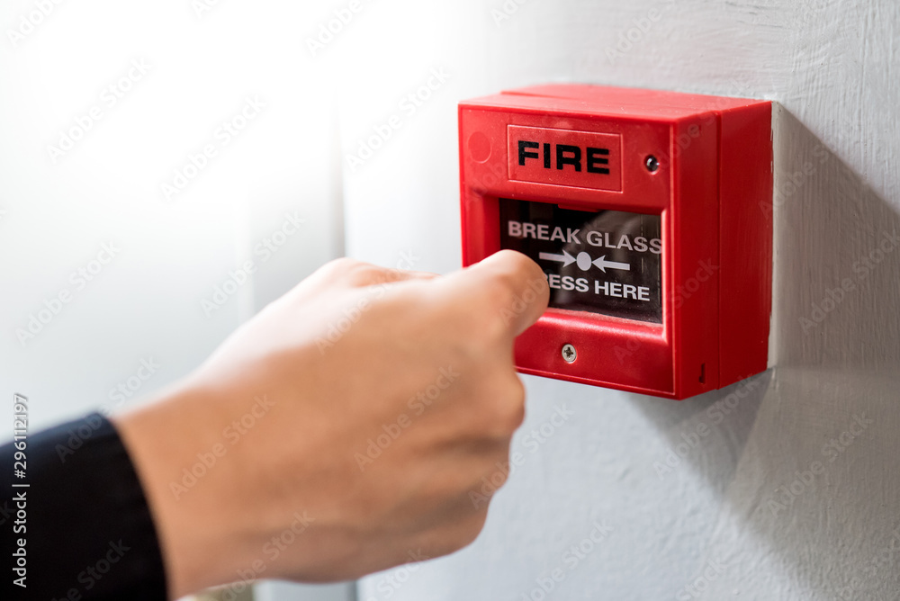 Male hand punching red fire alarm switch on concrete wall in public building. Industrial fire warning system equipment for emergency. - obrazy, fototapety, plakaty 