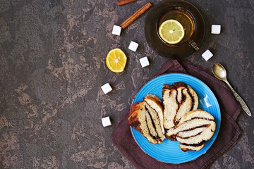 Wall Mural - Sliced twisted yeast cake with cocoa and cinnamon on a blue plate on a brown concrete background. Top view.