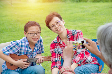 Wall Mural - Asian Senior male taking photo his wife and son by smart phone while they’re on vacation camping.