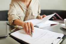 Close-up Of Young Woman Sitting At The Table And Pointing At Clipboard With Financial Report While Working At Office