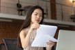 © fizkes - Focused young Asian businesswoman reading documents, using laptop