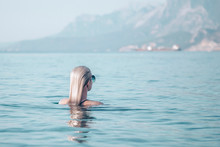Girl Swims In The Turquoise Sea. Back View Of A Girl With Smooth Wet Blond Hair. Travel And Relaxation Concept.