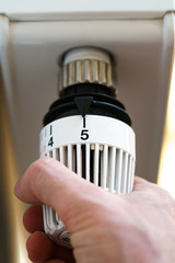 Hand of man adjusting radiator thermostat valve to number 5 icon, symbol for high heating costs or warm temperature setting