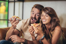 Couple Eating Pizza In Modern Cafe. They Are Laughing And Eating Pizza And Having A Great Time.
