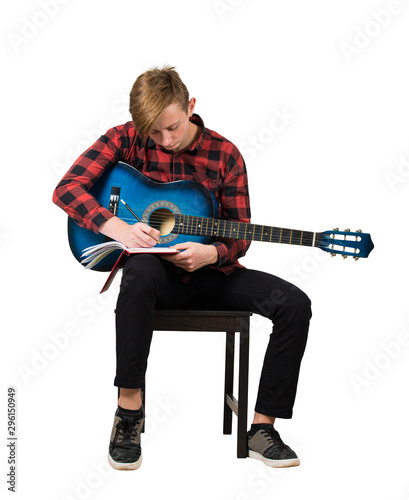 Fotomural Full length portrait of talented boy music composer with his trendy acoustic guitar seated on chair thinking to write a new song with chords in his notebook isolated over white background