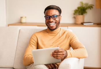 Poster - Afro Man Holding Digital Tablet Sitting On Couch At Home