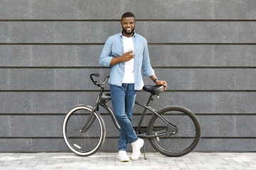 Portrait of handsome guy standing with bicycle and holding smartphone