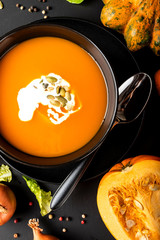 Wall Mural - Pumpkin cream soup with milk and pumpkin seeds in a black bowl on the black background. Close-up.