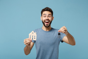 Wall Mural - Young surprised man in casual clothes posing isolated on blue wall background, studio portrait. People sincere emotions lifestyle concept. Mock up copy space. Holding in hands house and bunch of keys.