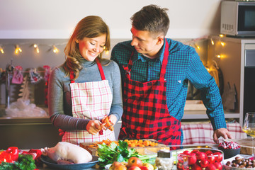 happy couple in aprons celebrating Christmas in the kitchen cooking christmas duck or Goose