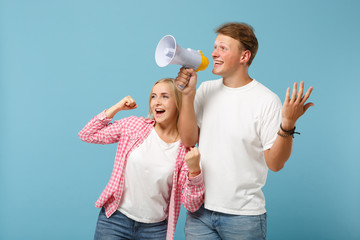 Young joyful couple two friends guy girl in white pink empty t-shirts posing isolated on pastel blue background. People lifestyle concept. Mock up copy space. Scream in megaphone doing winner gesture.