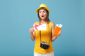 Traveler tourist woman in yellow casual clothes hat hold tickets gift card camera isolated on blue background. Female passenger traveling abroad travel on weekends getaway. Air flight journey concept.