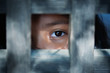 The blank stare of a child's eye who is standing behind what appears to be a wooden cage to convey captivity, or bondwoman.