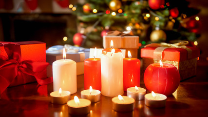 Wall Mural - Closeup image of lots of burning candles and gifts against glowing Christmas tree at living room