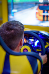 Wall Mural - Happy European boy playing racing simulator at indoor playground. Back view.