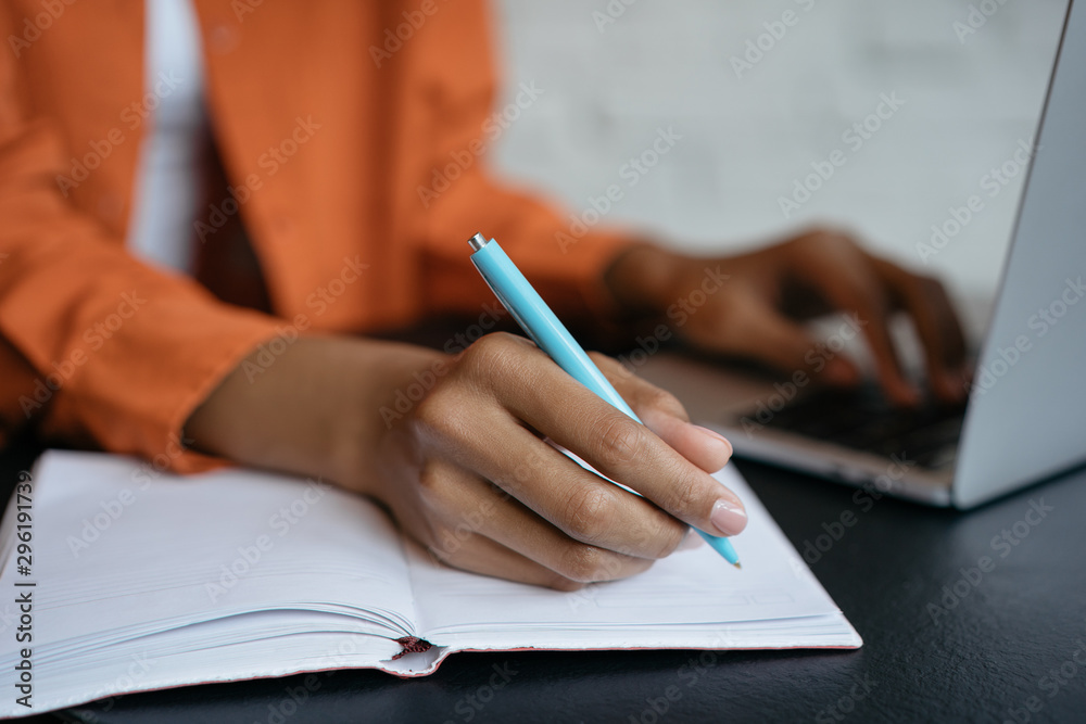 Closeup shot of university student hand using pen and writing in notebook, exam preparation, presentation, working project at workplace. Education concept. Woman taking notes, typing on keyboard  - obrazy, fototapety, plakaty 