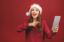 Ney Year Sale! Attractive Woman In Santa Hat And Sweater Holding Digital Tablet Isolated On Red.