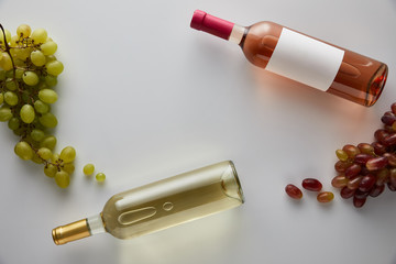 Wall Mural - top view of bottles with white and rose wine near grape on white background