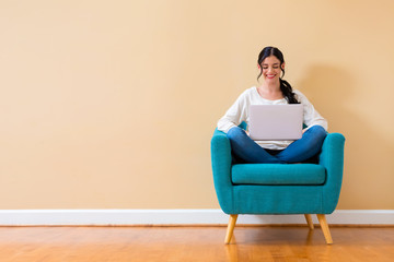 Wall Mural - Young woman with a laptop computer sitting in a chair