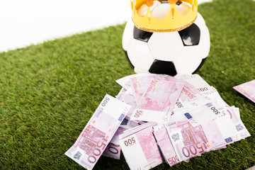 euro banknotes near soccer ball with paper crown on green grass isolated on white, sports betting concept