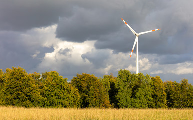 Wind turbine for generating electricity on a field in a rural area in Germany. Despite sunshine, dark and threatening clouds are in the sky. There will be rain.