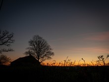 Silhouette Of A House Near Leafless Trees With A Sky At Sunset