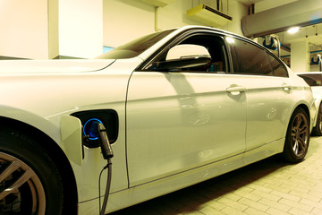 Wall Mural - Electric car charging on parking lot with electric car charging station on supermarket in city . Close up of power supply plugged into an electric car charging.	