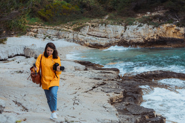 Wall Mural - woman walking by seaside and shooting landscape in yellow raincoat.