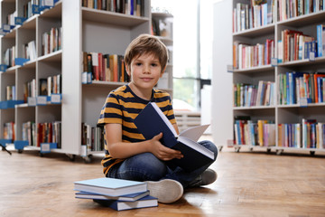 Wall Mural - Cute little boy reading book on floor in library