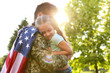 © New Africa - Father in military uniform with American flag holding his little daughter at green park