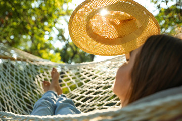 Young woman with hat resting in comfortable hammock at green garden, closeup