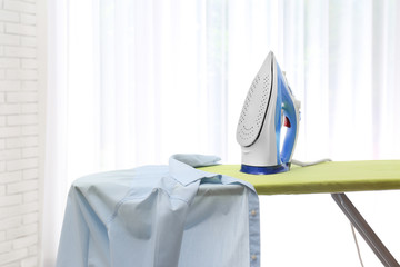 Board with modern iron and shirt at home. Laundry day